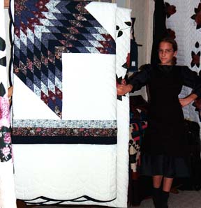 An Amish Girl displays an heirloom quilt.